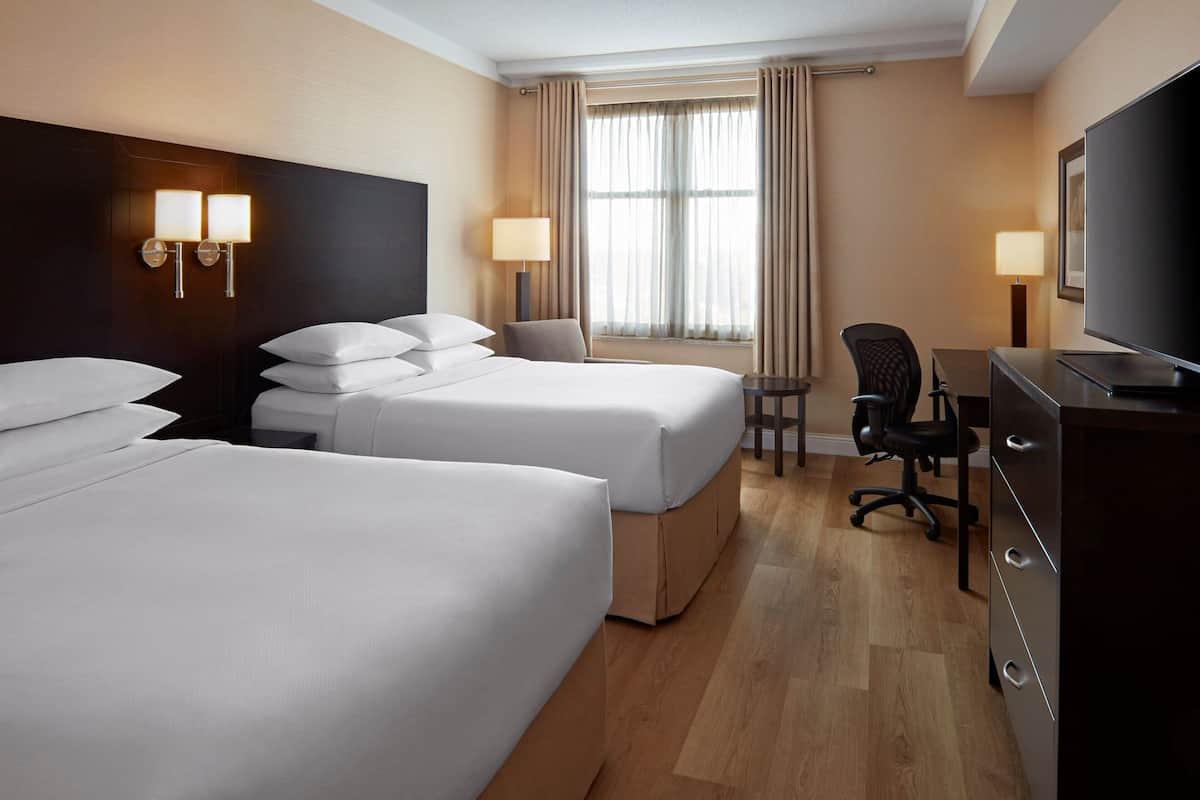 A hotel room with two beds, a desk, a chair, a television, and a window with curtains.
