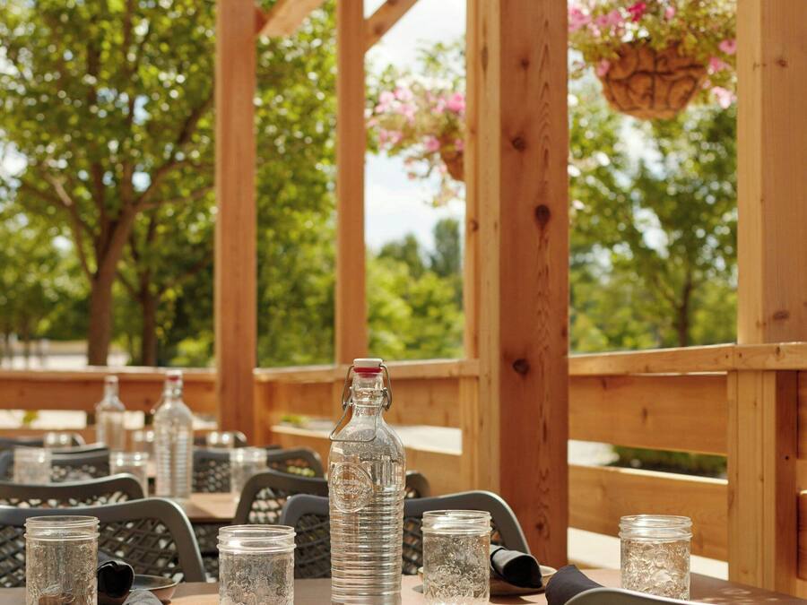 Une pergola en bois installée à l’extérieur, avec des tables et des chaises, un ciel dégagé et des paniers de fleurs suspendus.