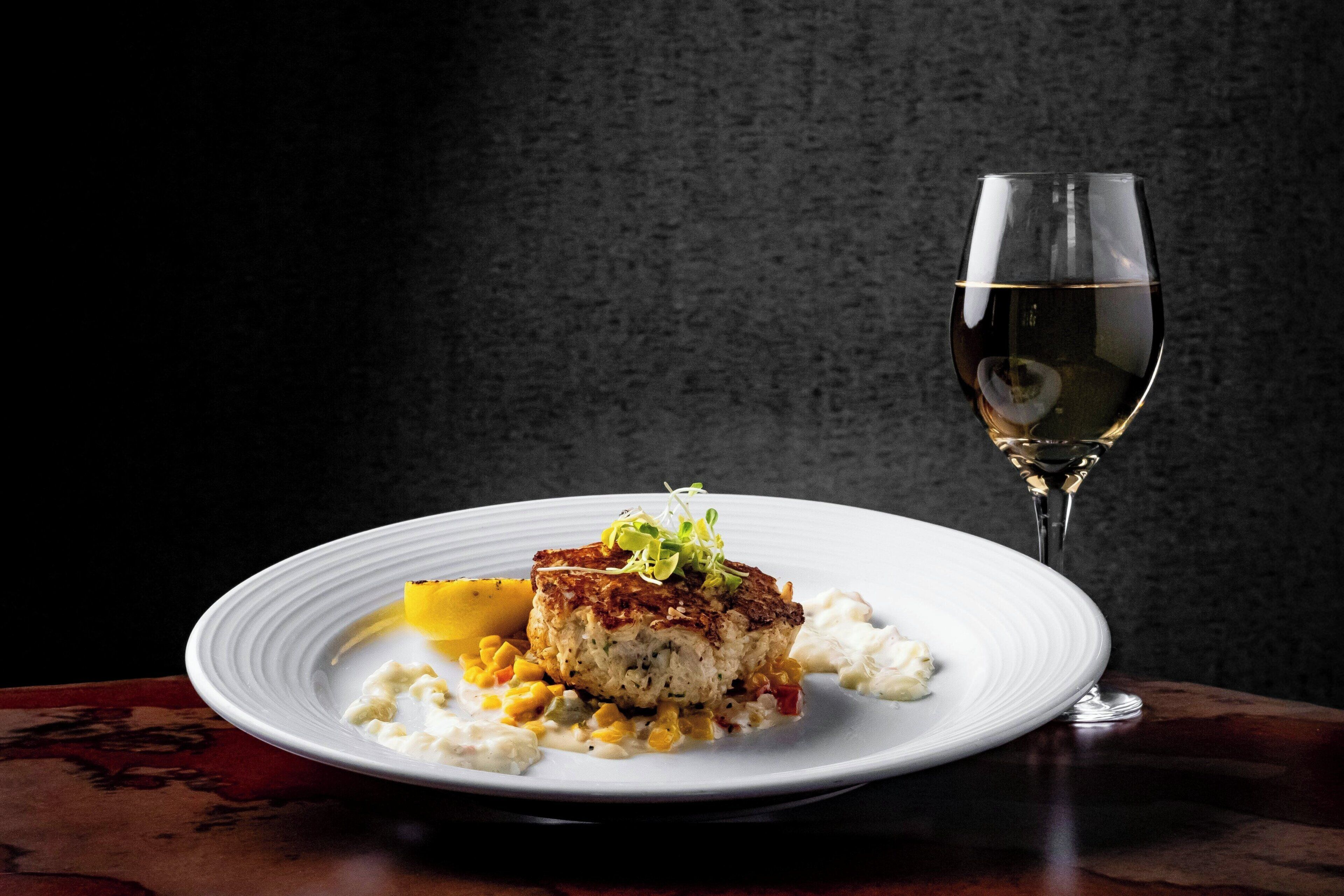A plate of food with a glass of white wine on a dark background.