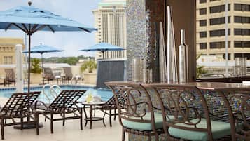 A poolside area with lounge chairs, umbrellas, and a bar.