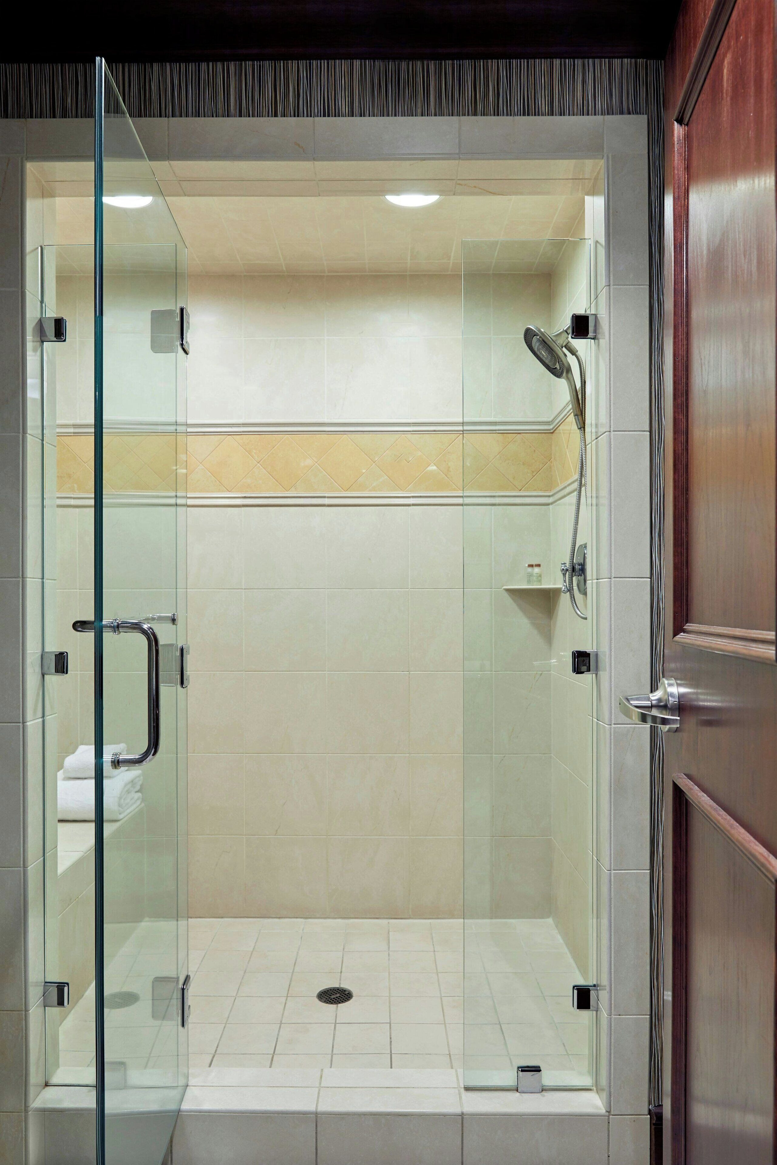 Une douche fermée par des parois de verre, avec un sol carrelé et une porte en bois.