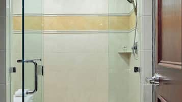 Une douche fermée par des parois de verre, avec un sol carrelé et une porte en bois.