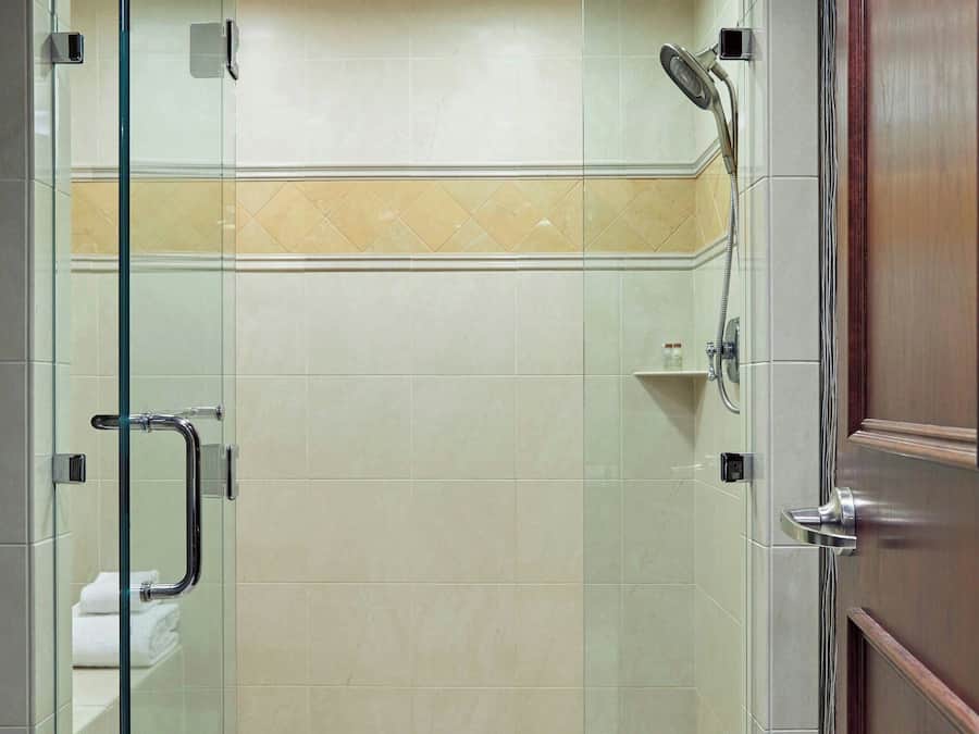 Une douche fermée par des parois de verre, avec un sol carrelé et une porte en bois.