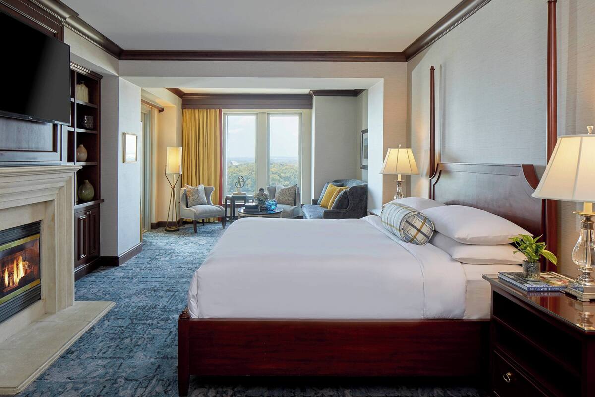 A hotel room with a large bed, a fireplace, a television, and a view of the outdoors.