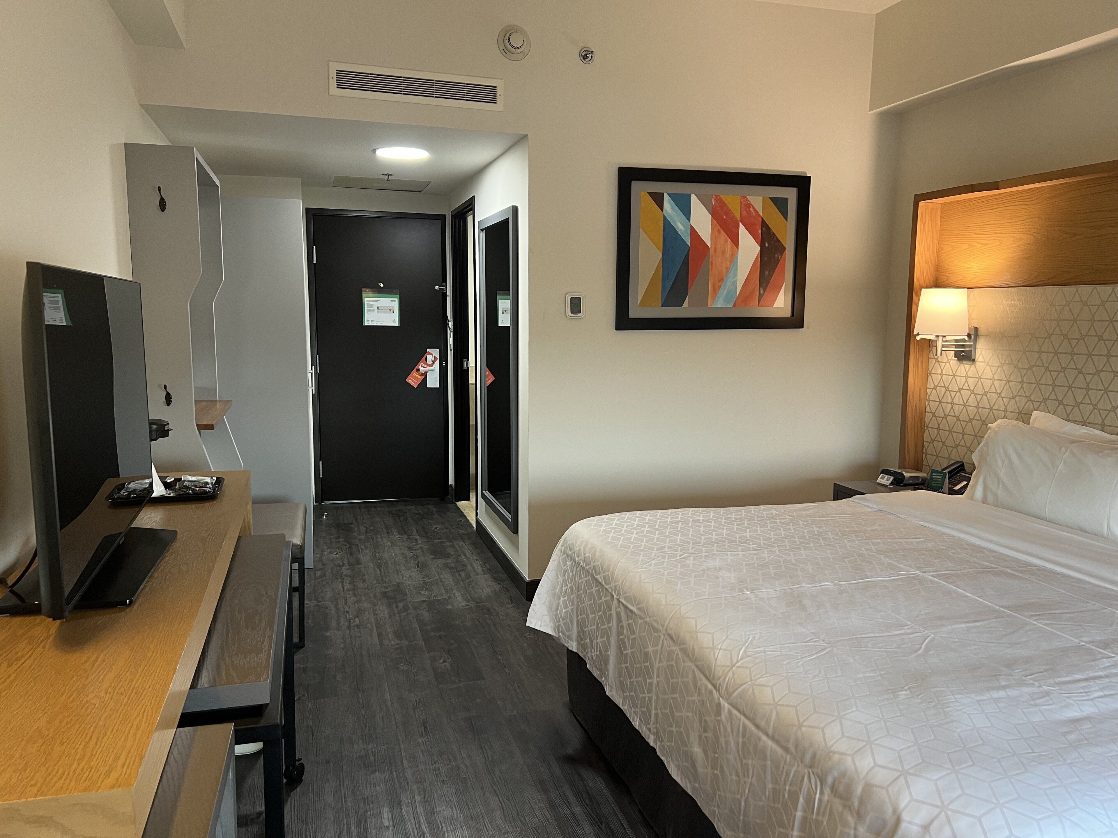 A hotel room with a bed, a desk with a computer, a TV, and a painting on the wall.
