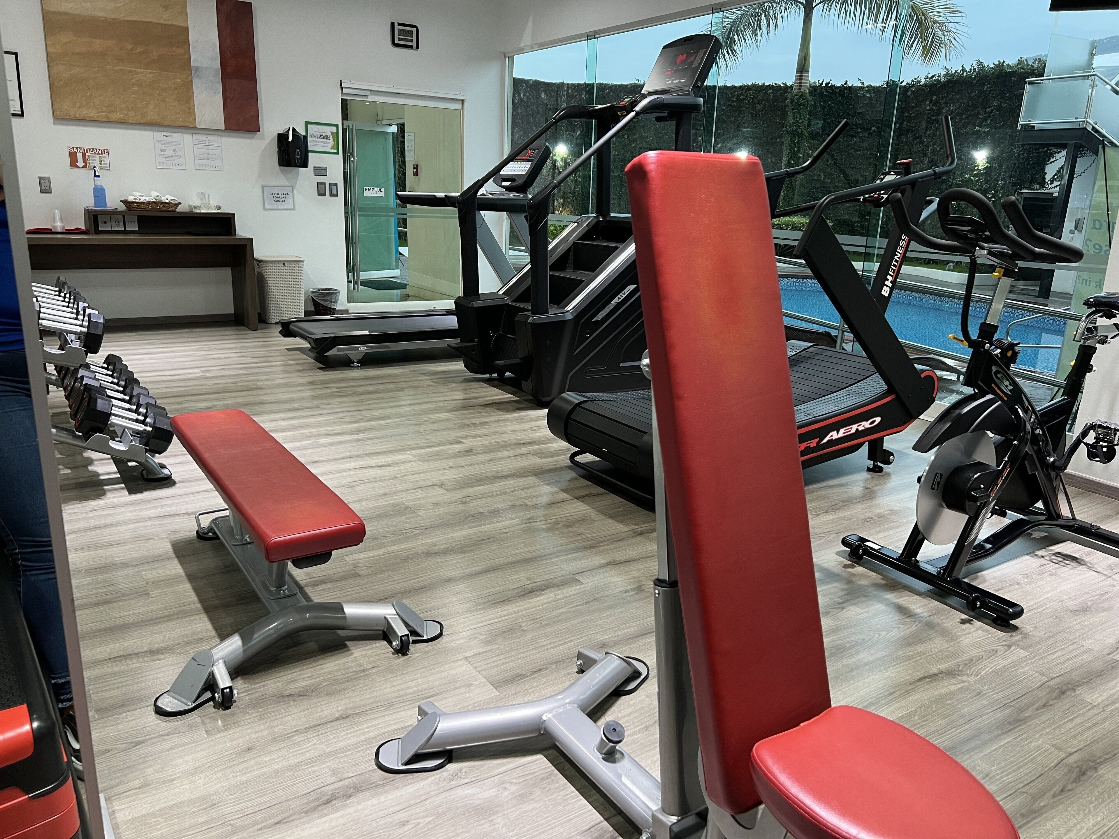 A gym with exercise equipment, a bench, and a view of a swimming pool.