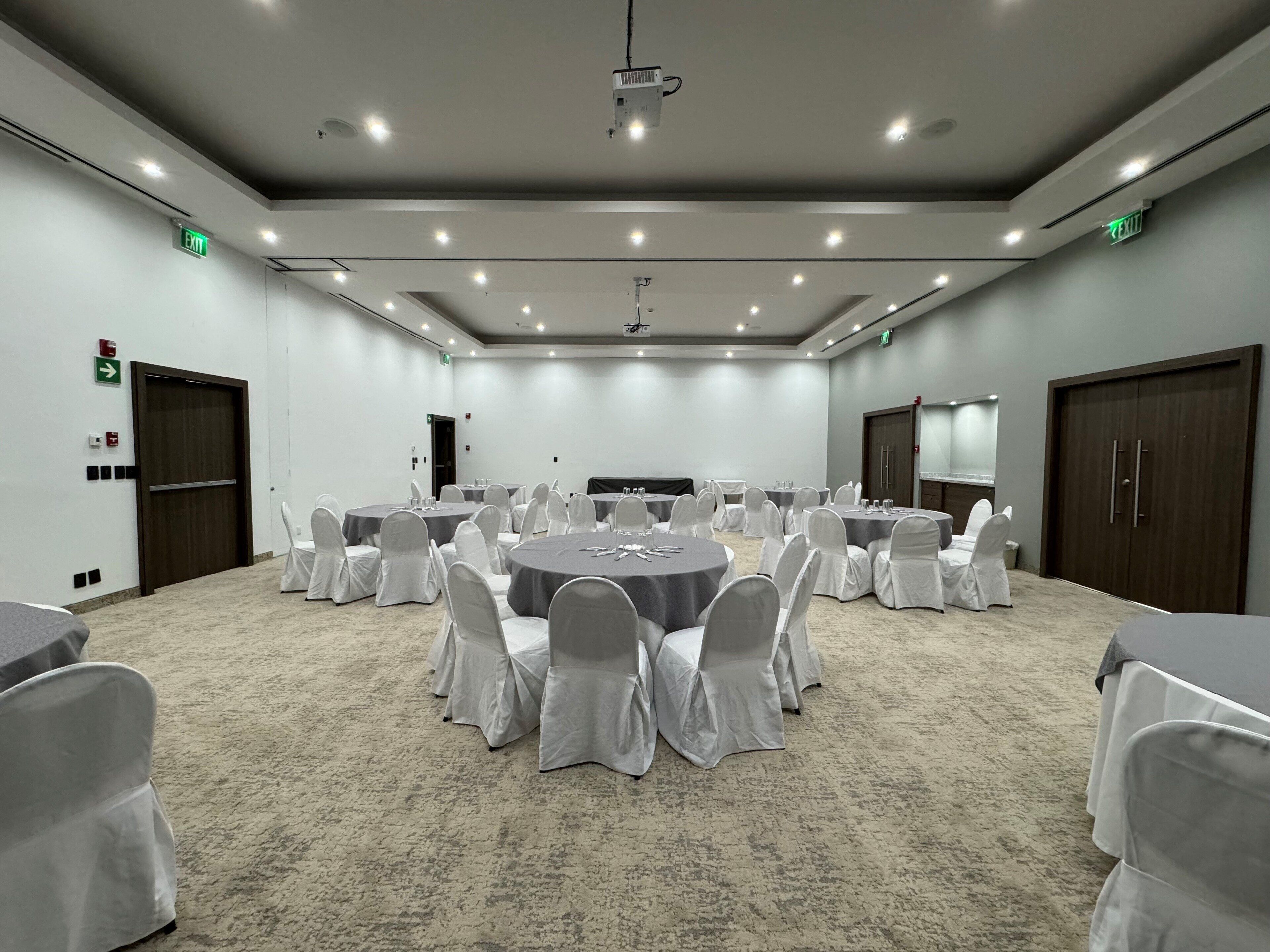 A conference room with round tables, white chairs, and a projector screen.