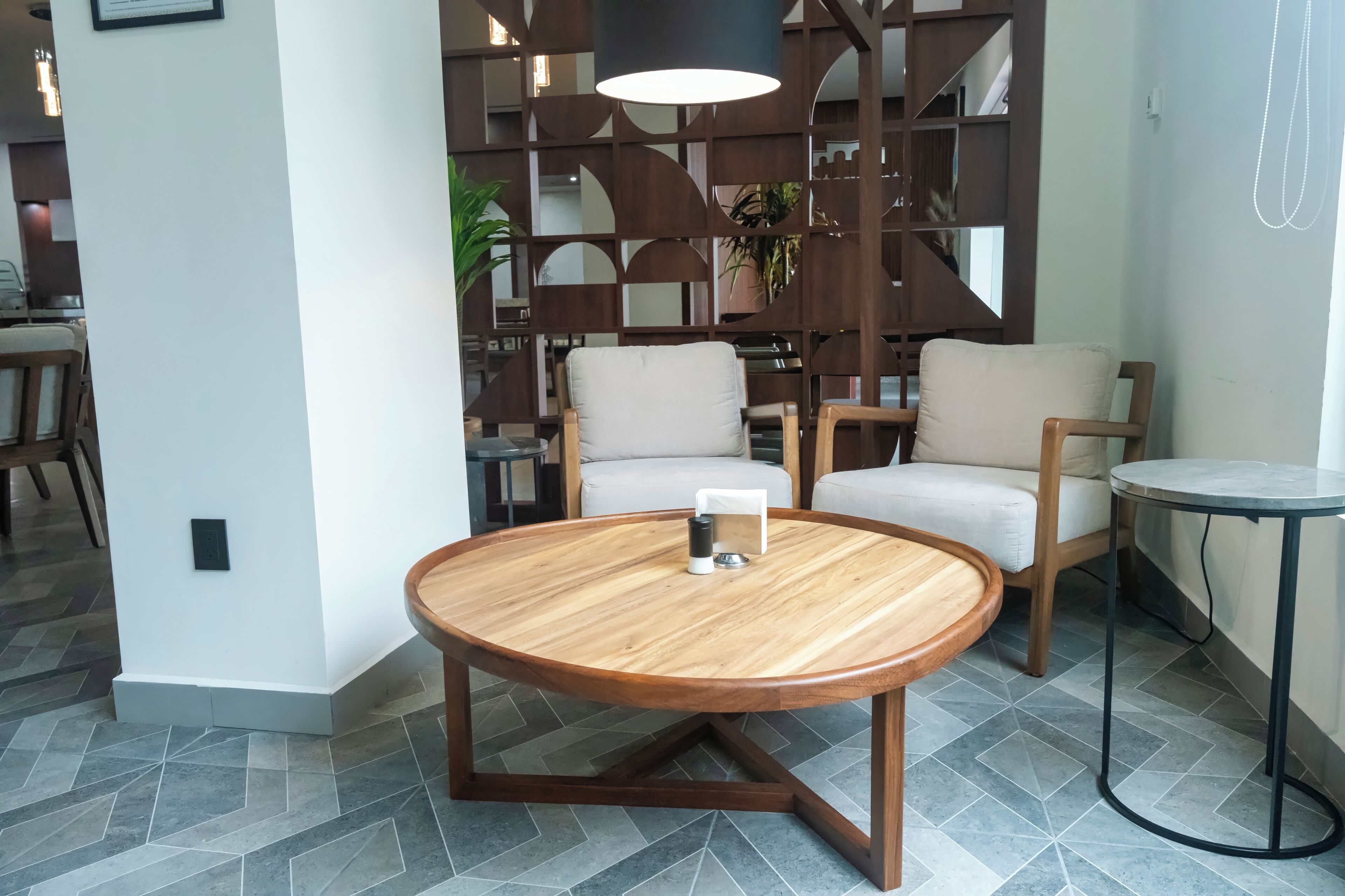 A modern room with a round wooden table, two cushioned chairs, a small round table, and a decorative wall panel.