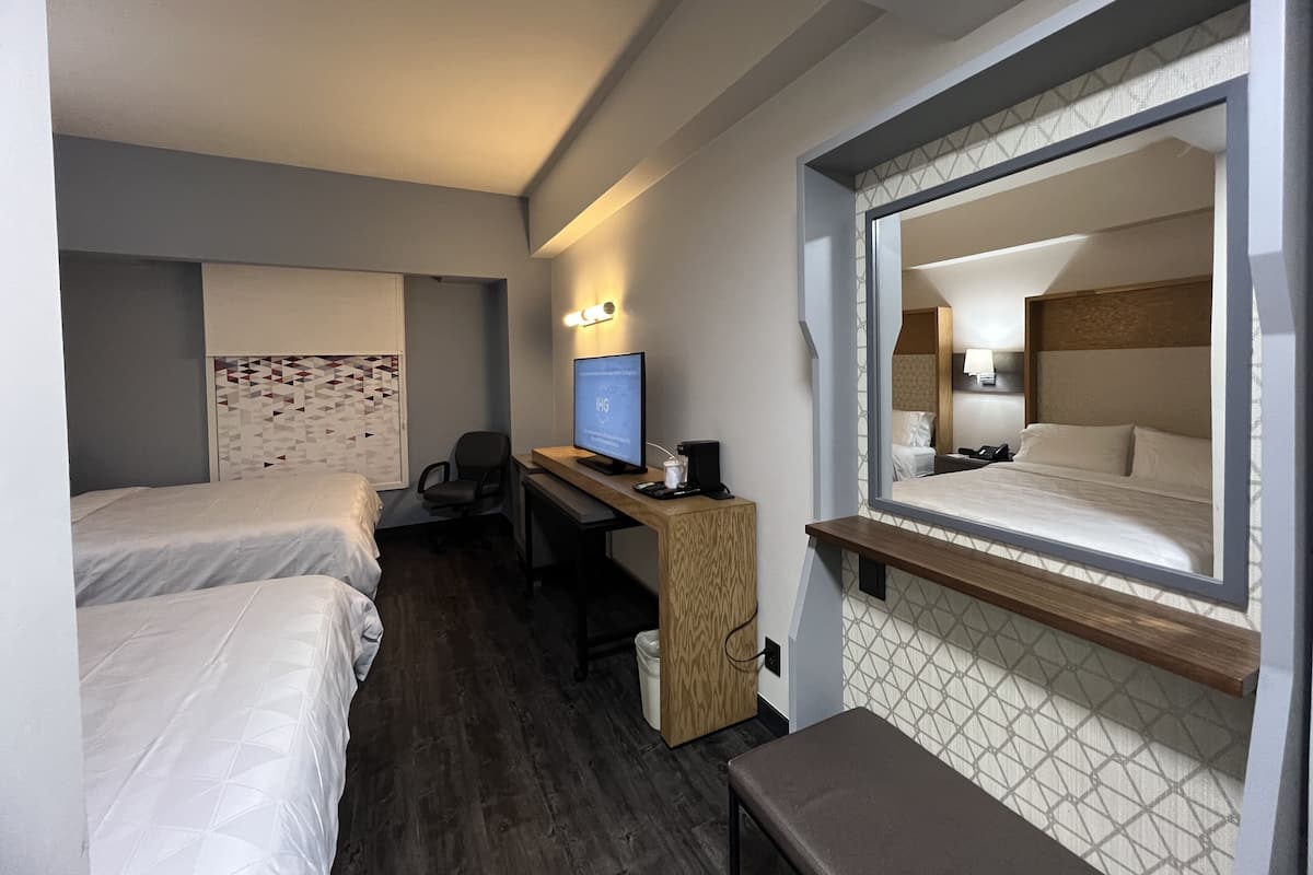 A hotel room with two beds, a desk with a computer, and a large mirror reflecting the room.