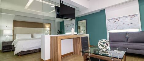 A modern hotel room with a bed, a desk, a sofa, and a TV.