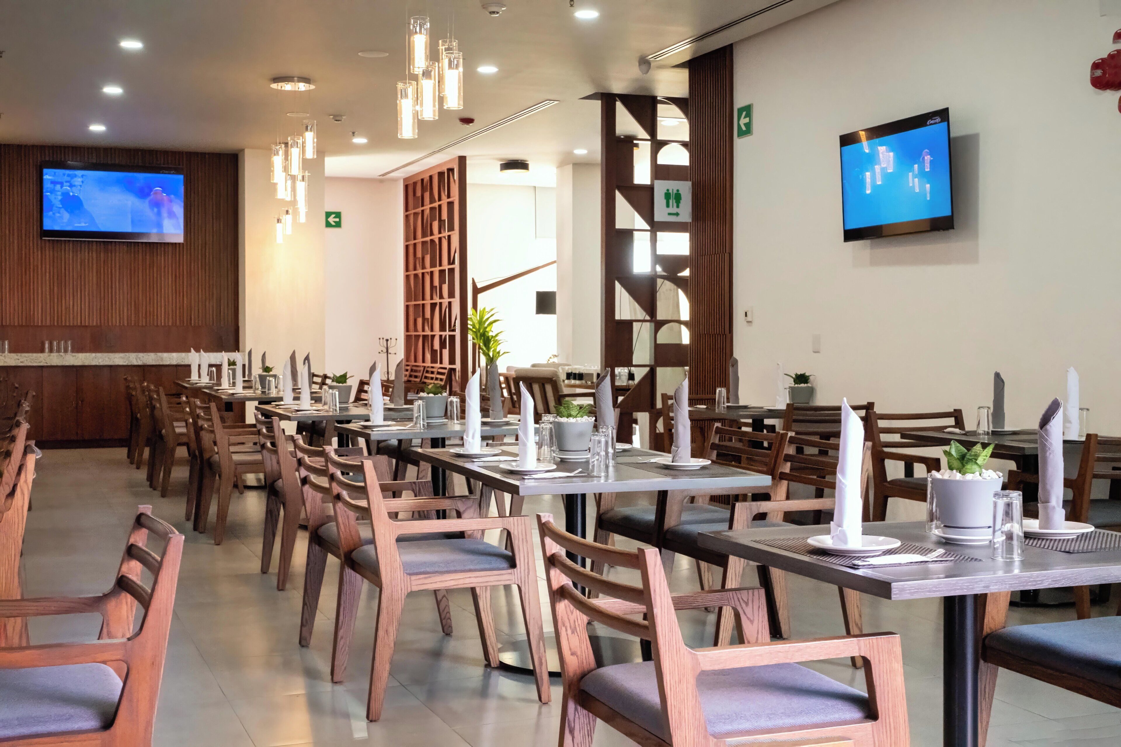 A dining area with wooden chairs and tables, a TV screen, and a plant on the wall.