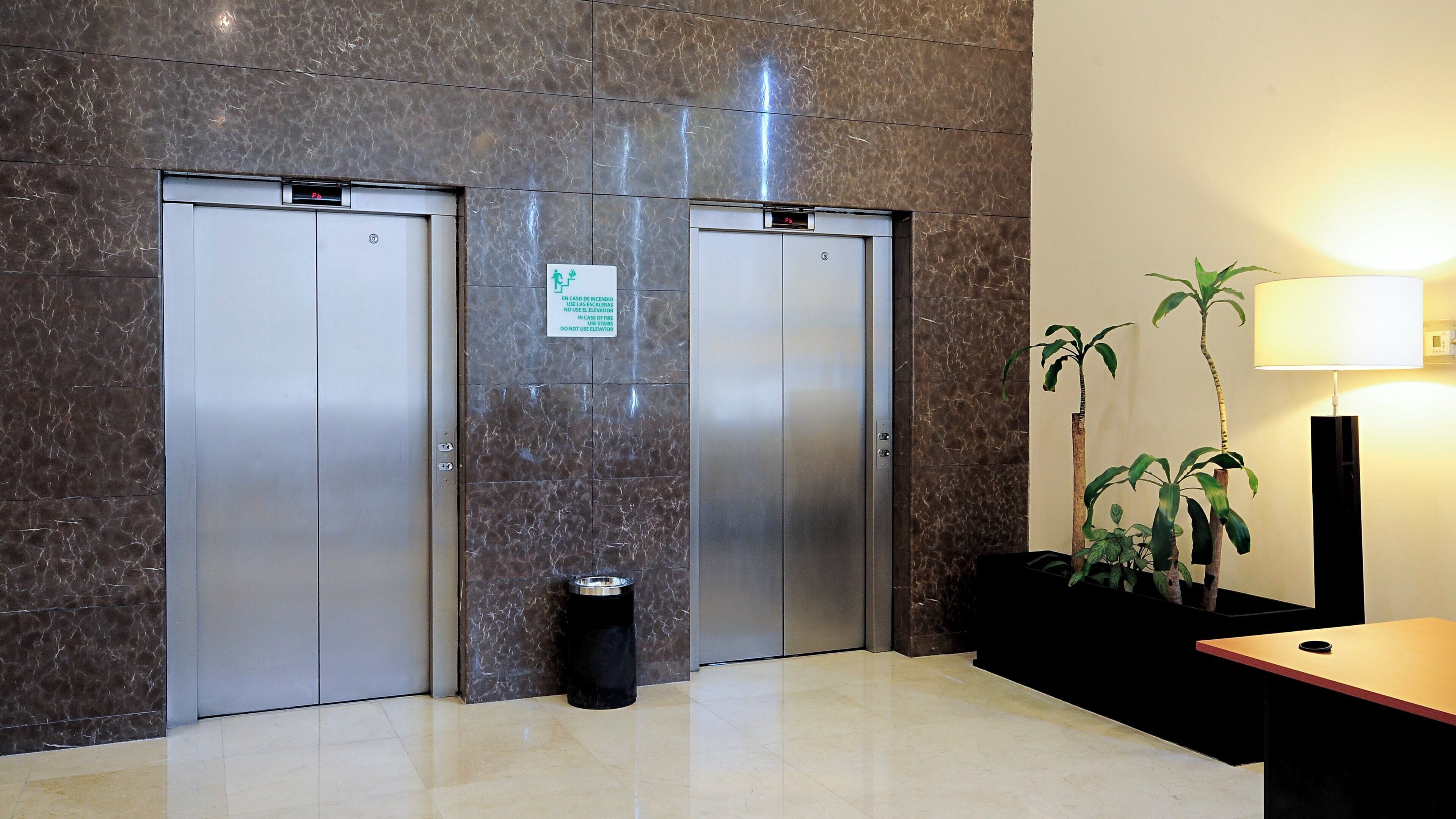 Dos ascensores con pared de mármol y un cartel que indica su uso.