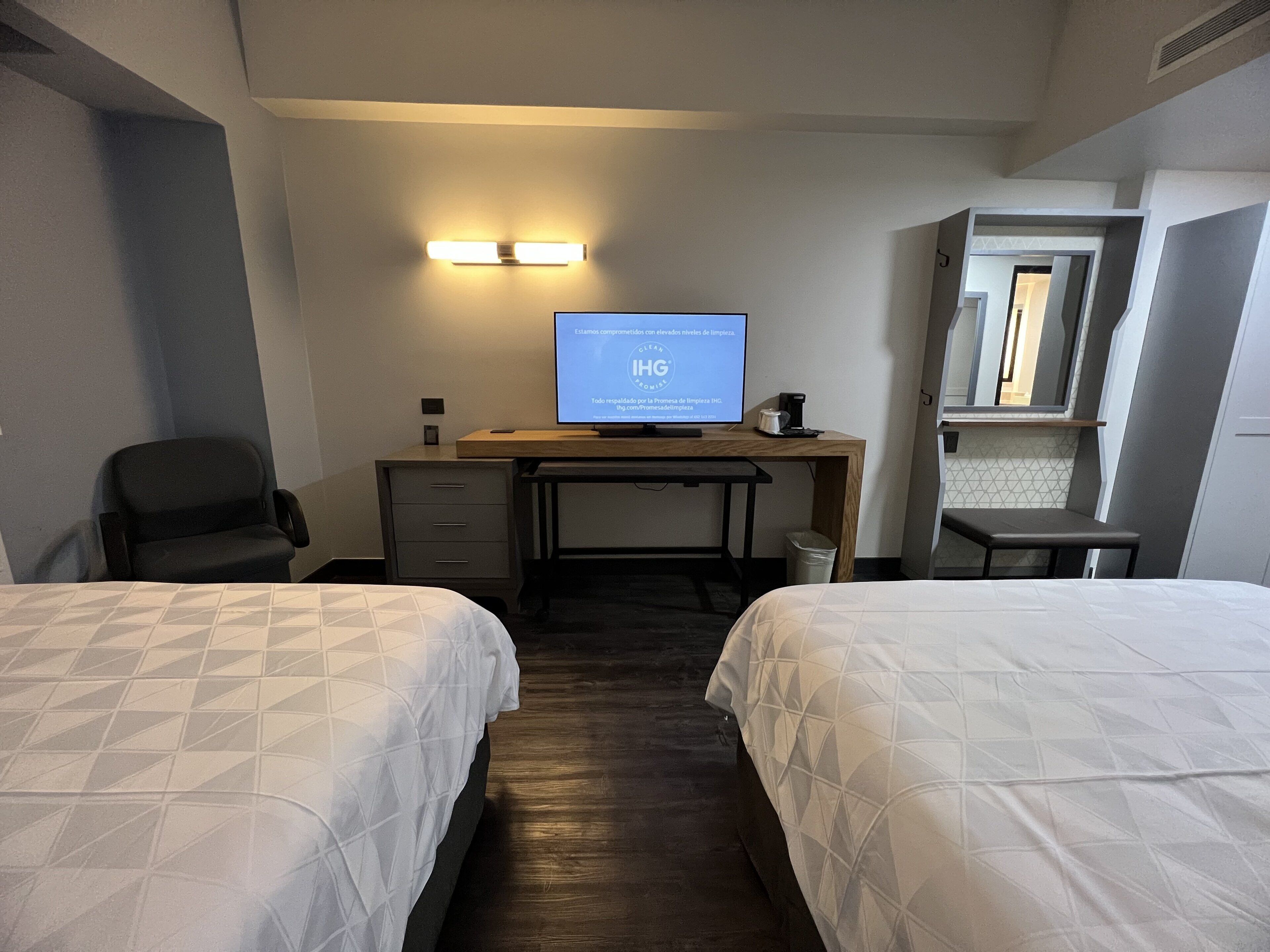 A hotel room with two beds, a desk with a computer, a chair, and a mirror.