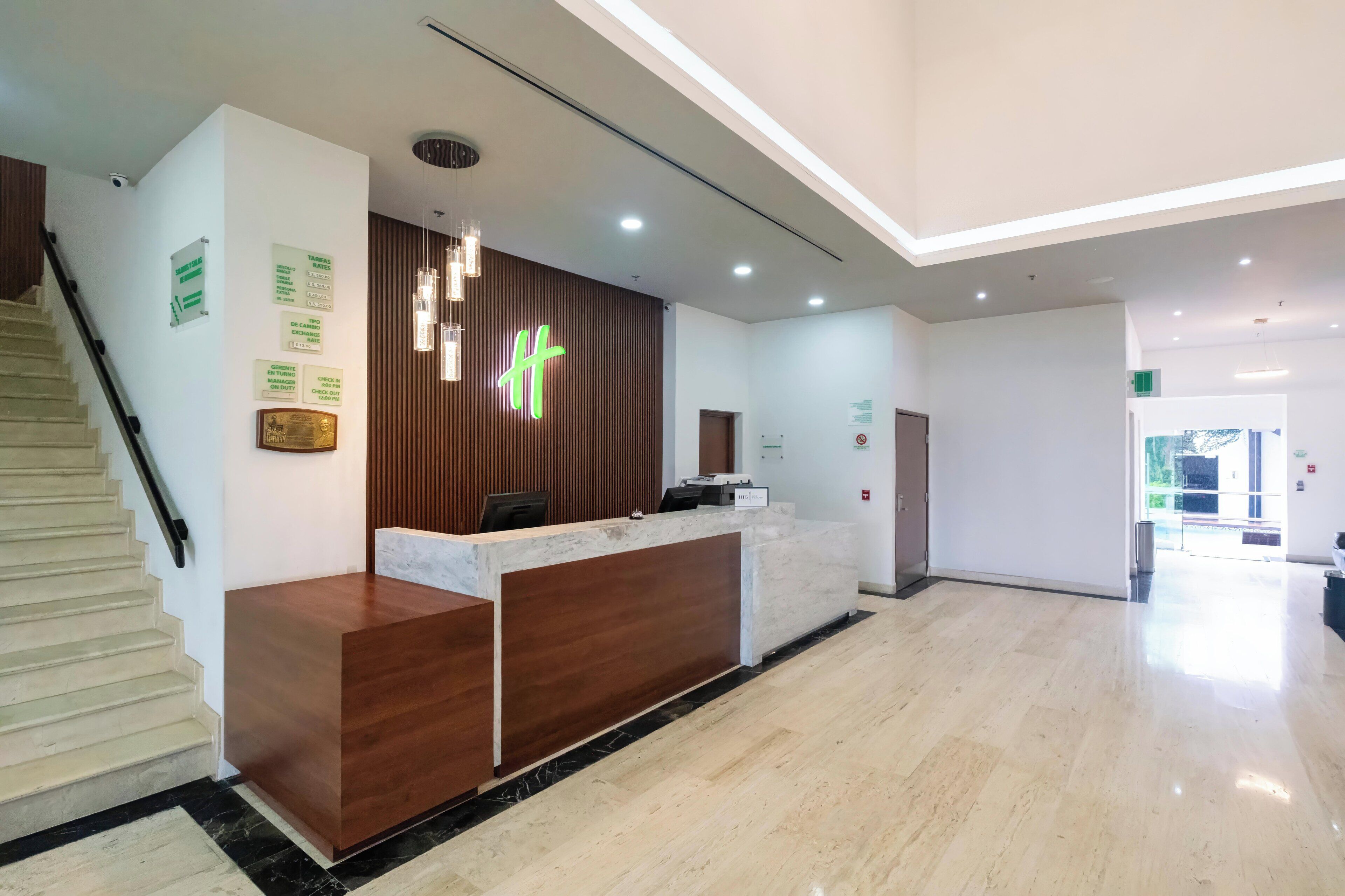 A modern reception area with a wooden reception desk, a staircase on the left, and a clean, well-lit interior.
