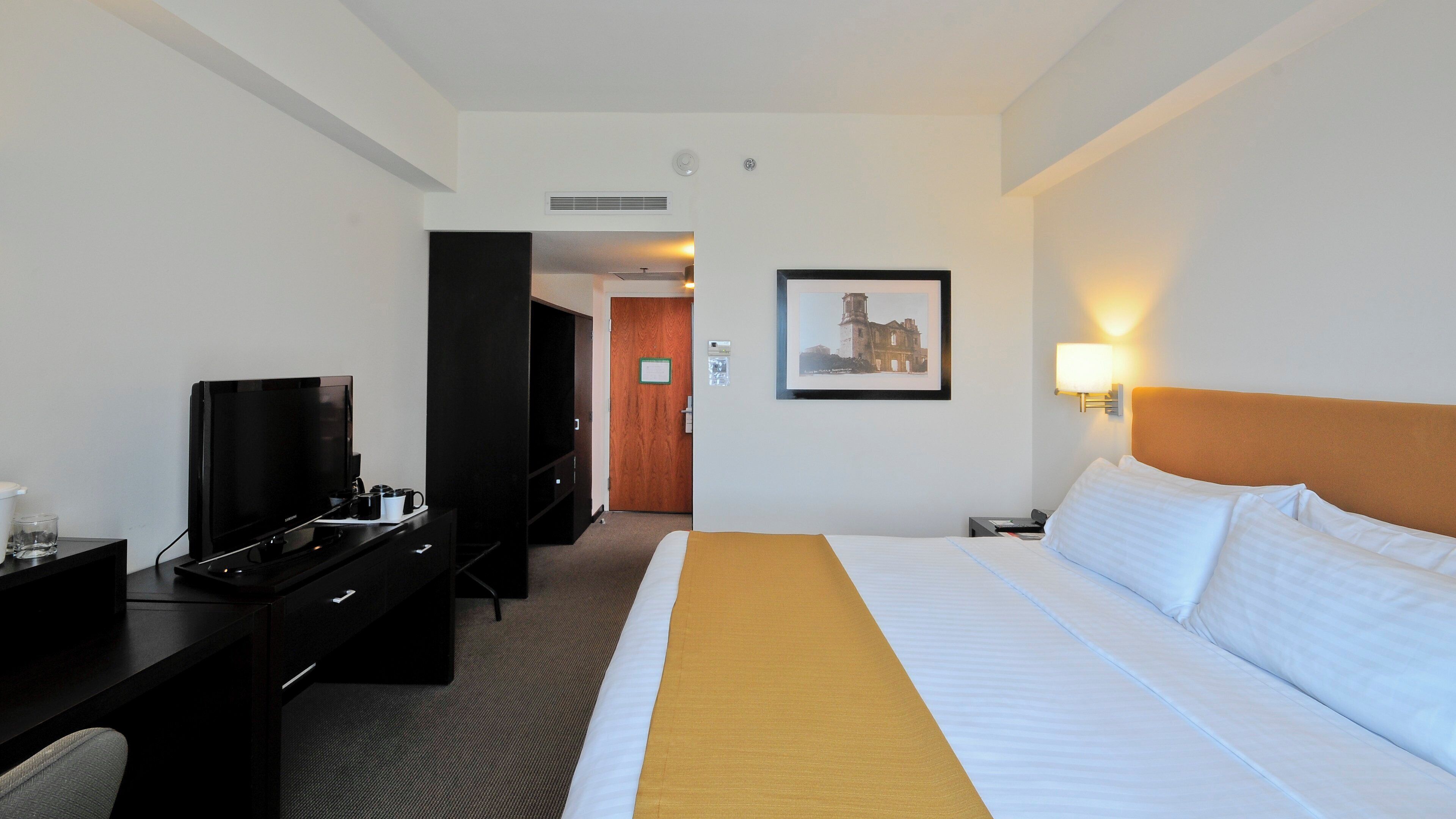 Une chambre d’hôtel avec un lit, un bureau avec une télévision, une chaise et une lampe.
