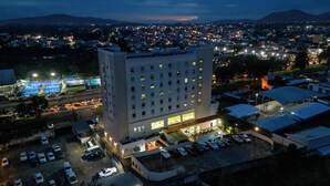 Un hotel de gran altura con varios pisos, un área de estacionamiento y vista a un paisaje urbano al anochecer.