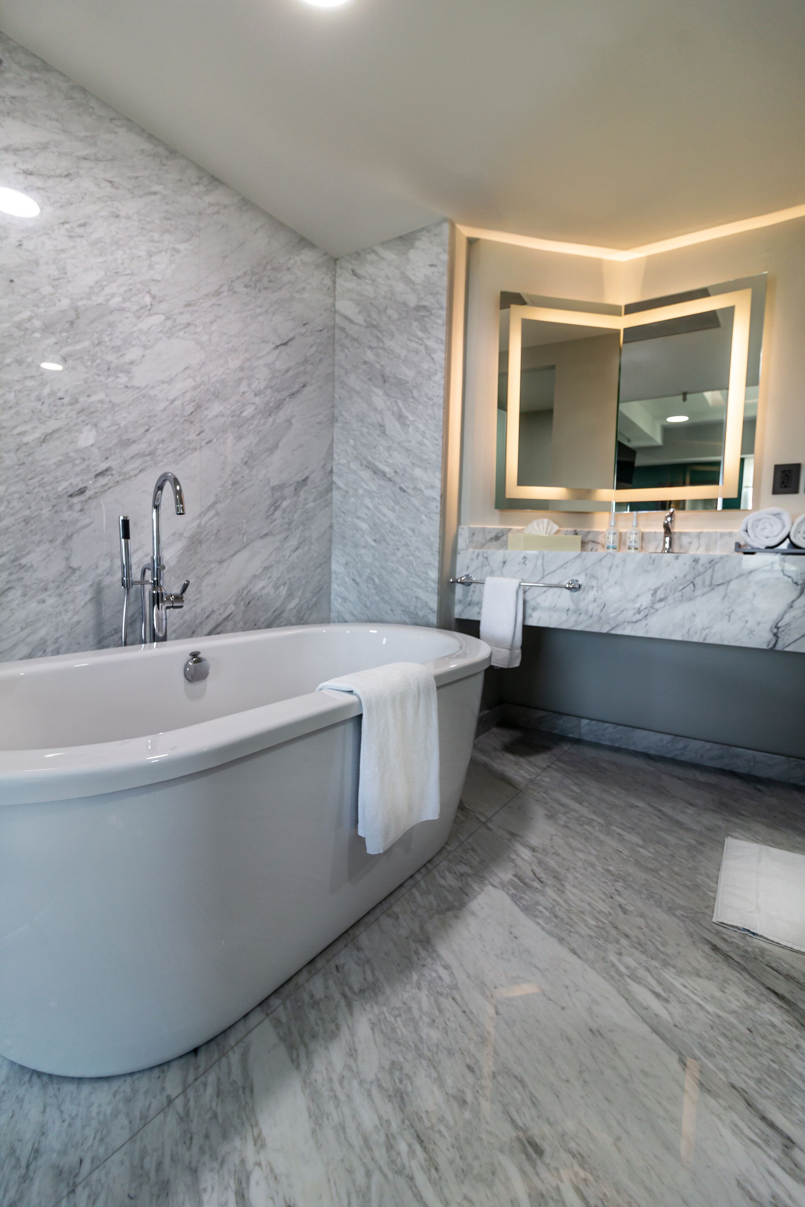 Un baño moderno con una bañera independiente, un espejo grande y paredes de mármol.