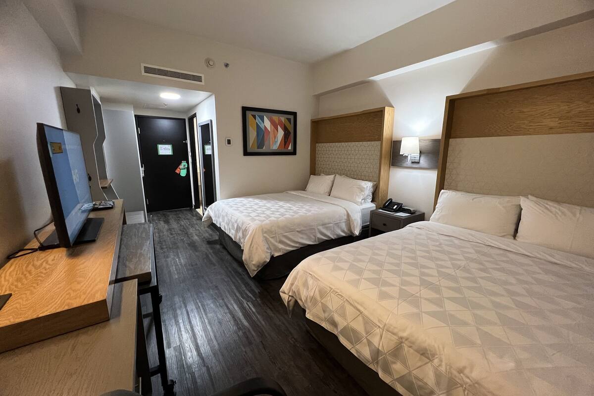Habitación de hotel con dos camas, un escritorio con una computadora y una puerta que da a otra habitación.