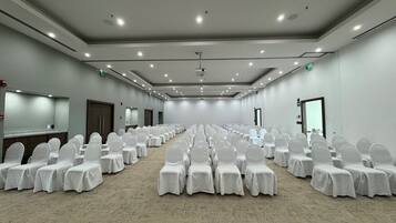 A conference room with rows of white-covered chairs and tables, a projector screen, and a carpeted floor.