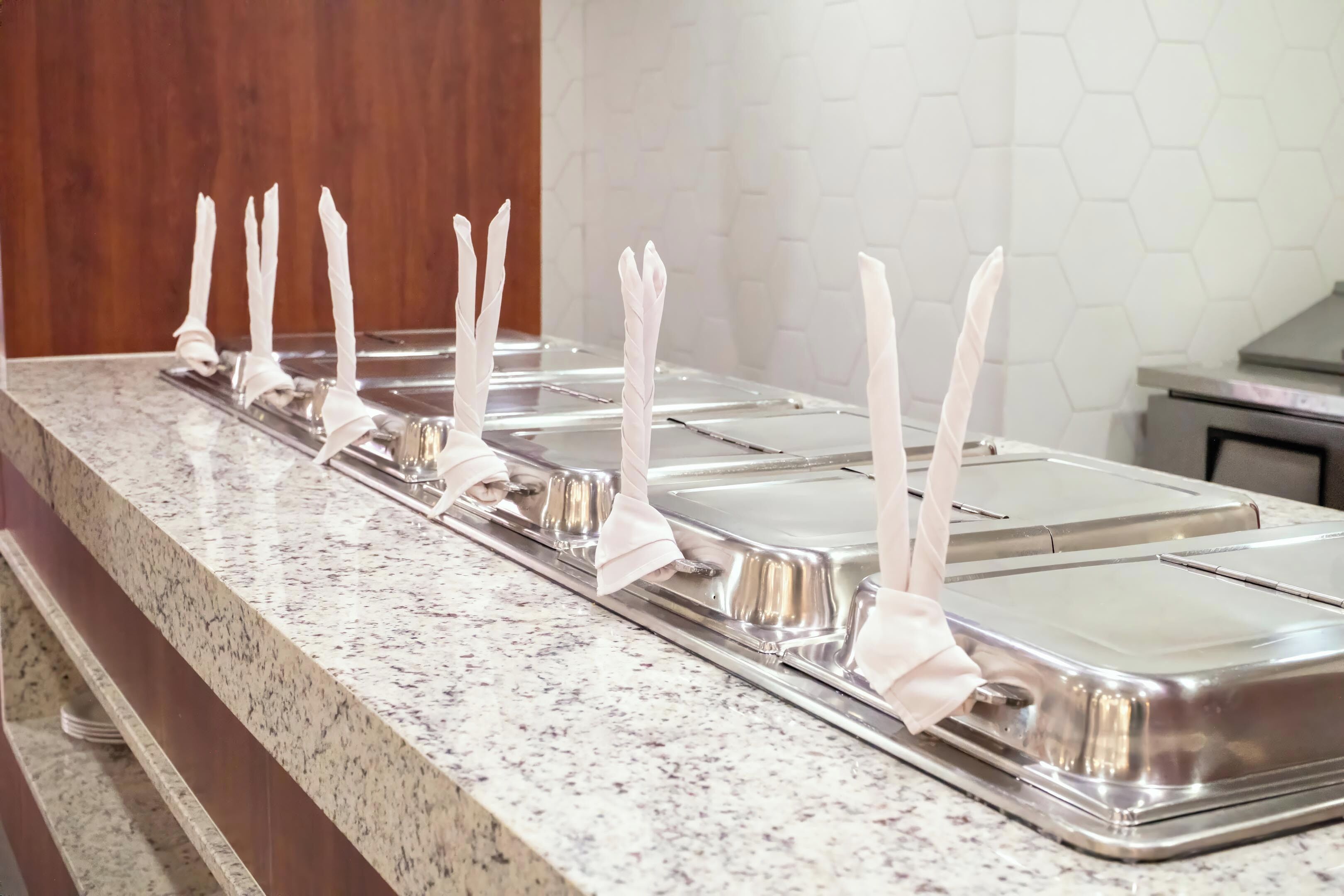 A buffet line with multiple stainless steel serving trays, each with a white napkin holder.