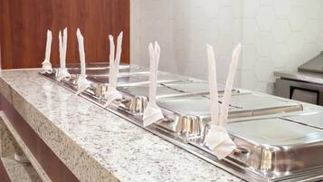 A buffet line with multiple stainless steel serving trays, each with a white napkin holder.