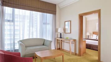 Ein Hotelzimmer mit einer Couch, einem Tisch, einem Schreibtisch mit Lampe, einem Bett und einem Spiegel.