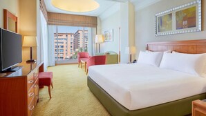 A hotel room with a large bed, a TV, a desk, a chair, and a view of buildings. - Holiday Inn Cairo Citystars by IHG (Cairo)