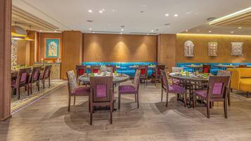 A restaurant with round tables, blue cushioned booths, and patterned chairs.