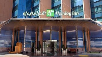 A Holiday Inn hotel entrance with a glass facade, a covered entrance area, and a sign in both English and Arabic.
