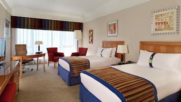 A hotel room with two beds, a desk, a chair, a TV, and artwork on the walls.