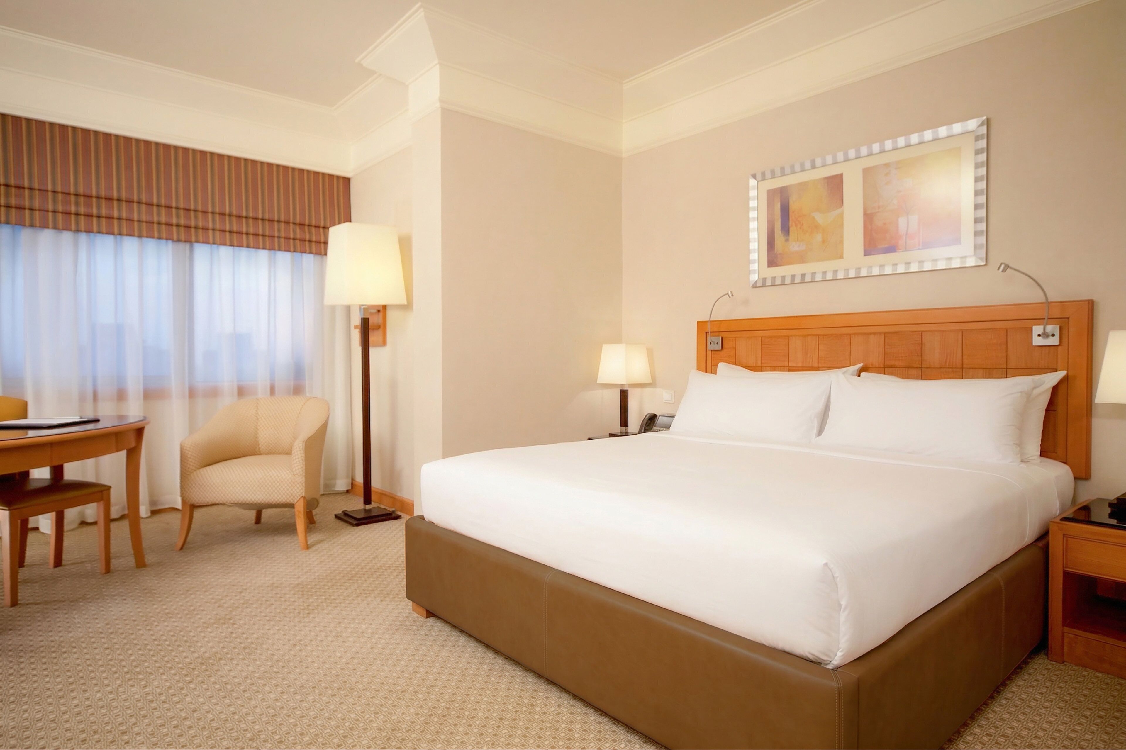 A hotel room with a large bed, a desk, a chair, a lamp, and a mirror on the wall.