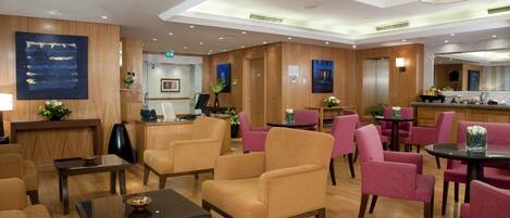 A hotel lobby with wooden paneling, multiple seating areas, a reception desk, and a dining area with a buffet.