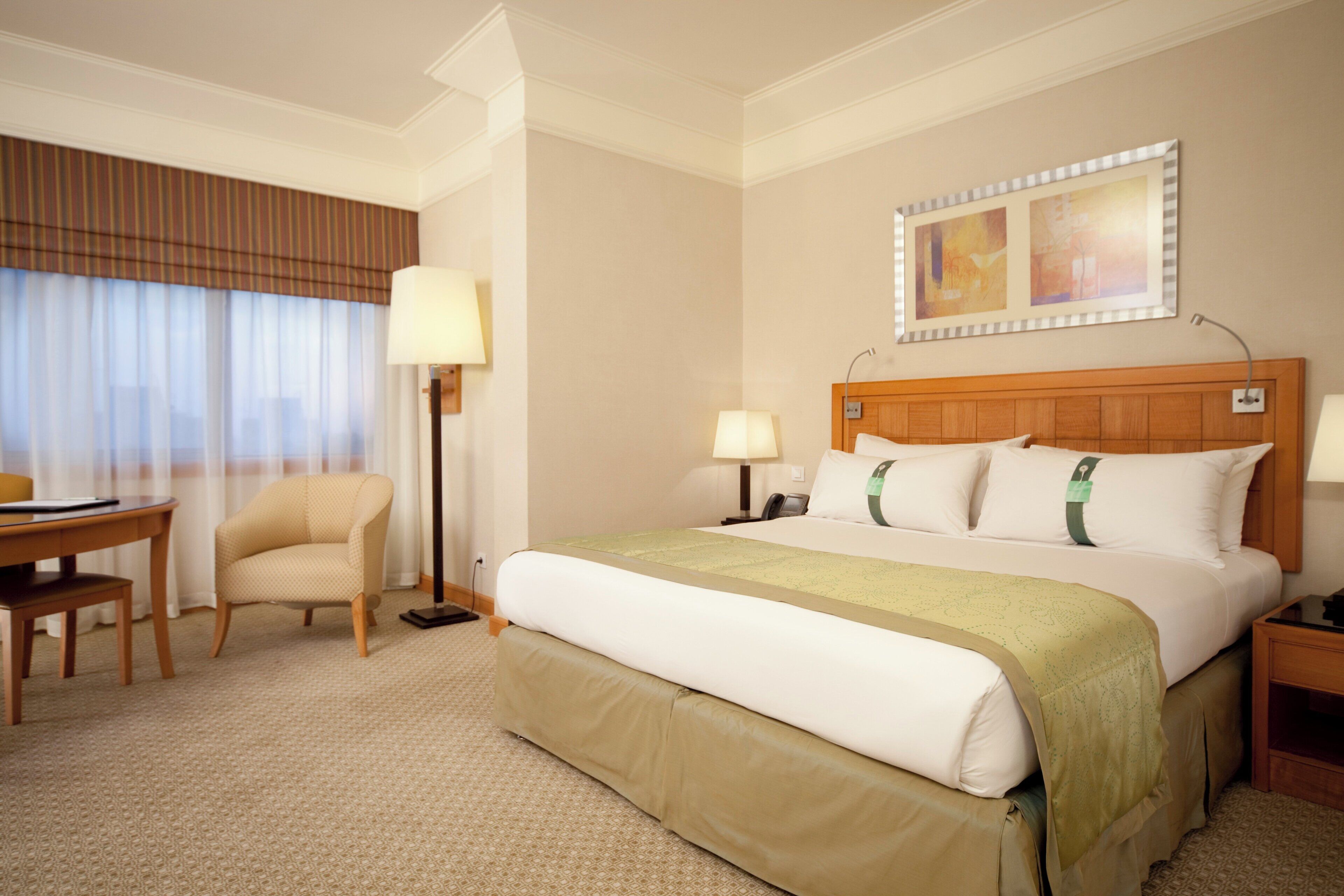 Une chambre d’hôtel comprenant un lit, des tables de chevet, un bureau, une chaise, une lampe, un téléphone et une fenêtre avec des rideaux.