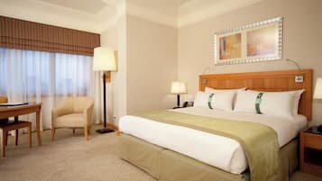 A hotel room with a bed, bedside tables, a desk, a chair, a lamp, a telephone, and a window with curtains.