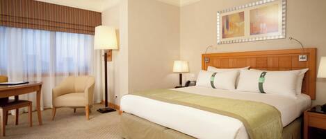 A hotel room with a bed, bedside tables, a desk, a chair, a lamp, a telephone, and a window with curtains.