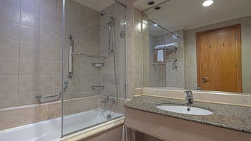 A modern bathroom with a glass-enclosed shower, a marble sink, and a wooden door.