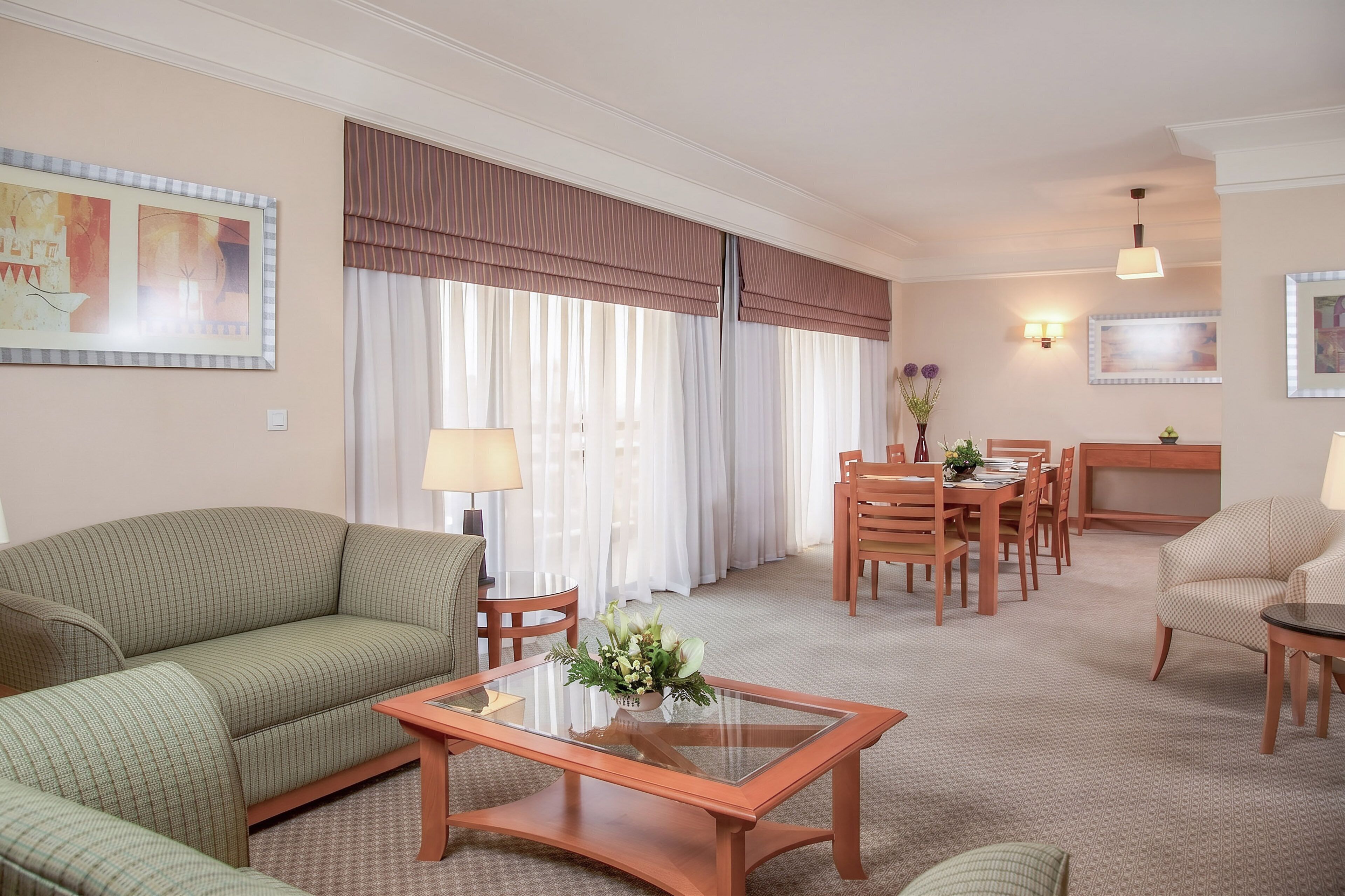 Une chambre d’hôtel comprenant un canapé, une table basse en verre, une table à manger avec des chaises, une lampe et un téléviseur.