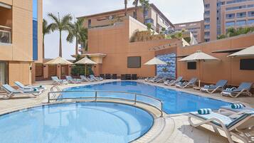 Una piscina al aire libre, sombrillas, sillones reclinables de piscina