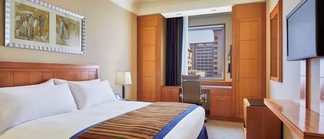 Habitación de hotel con una cama grande, un escritorio, una silla, un televisor y una ventana con vistas a edificios.