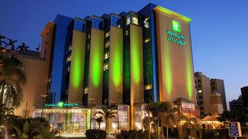 A multi-story Holiday Inn hotel with illuminated signage, a visible entrance, and a parking sign indicating underground parking.
