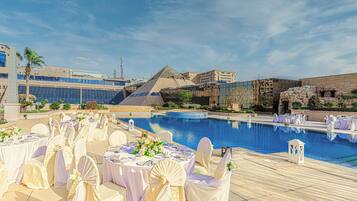 A poolside area with tables set for a wedding, overlooking a large pool and modern buildings.