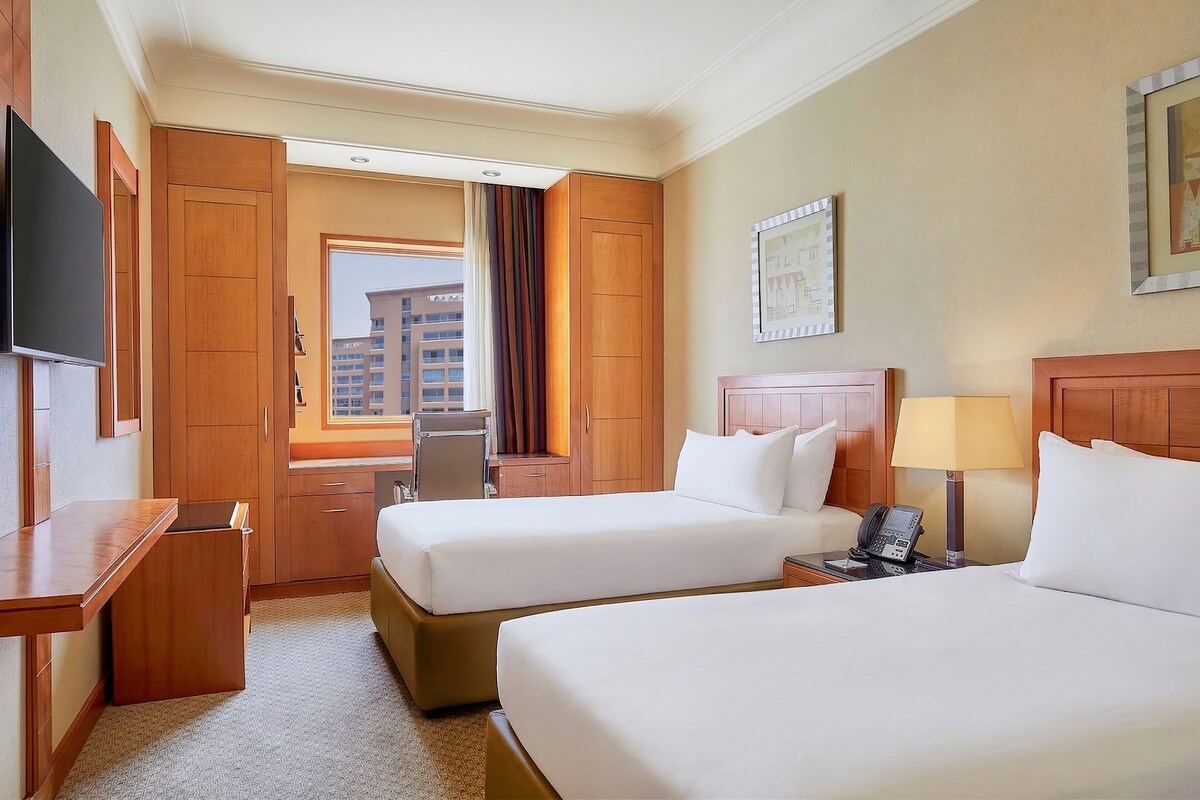 Une chambre d’hôtel avec deux lits, un bureau, une chaise, un téléphone et une télévision.