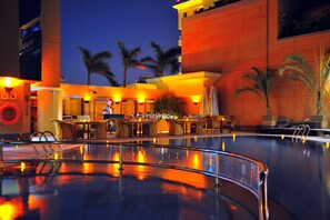 A pool area with a bar and seating, palm trees, and a building with warm lighting. - Holiday Inn Cairo Citystars by IHG (Cairo)