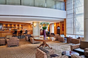Un hall d’hôtel comprenant un bar, des espaces aménagés avec des sièges et une grande fenêtre laissant entrer la lumière naturelle.