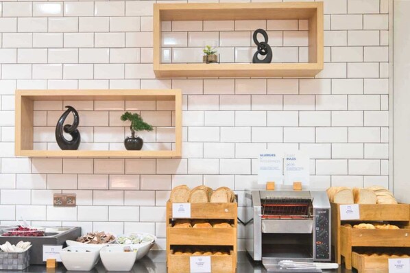 Een bakkerijdisplay met brood en gebak, een koffiemachine en een bordje over allergieën en intoleranties.