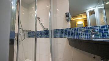 A bathroom with a glass shower enclosure, white tiled walls, and a blue-tiled backsplash.