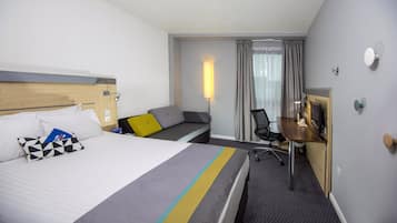 Una habitación de hotel con cama, escritorio, silla y ventana con cortinas.