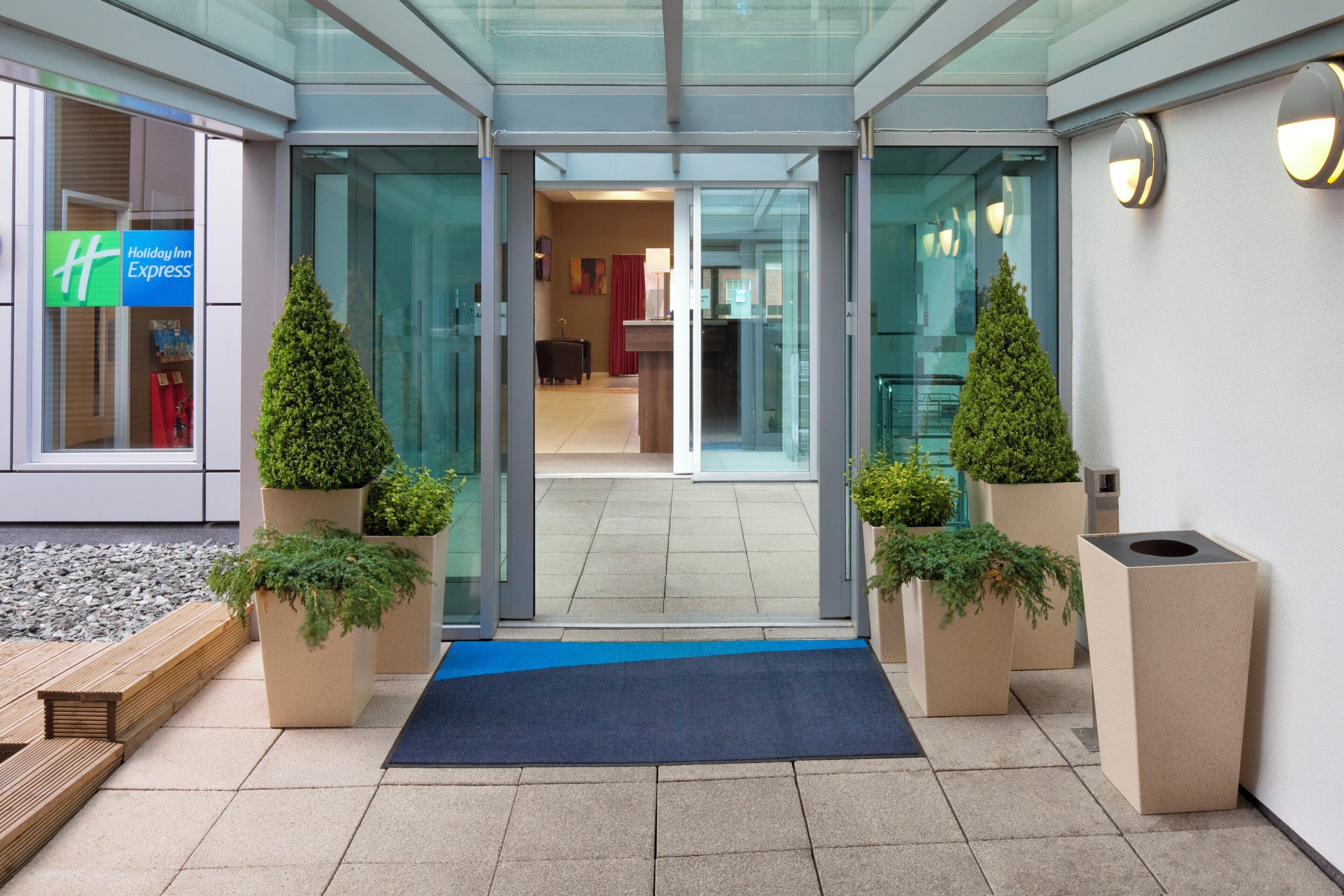 A hotel entrance with a glass door, a blue mat, and potted plants.