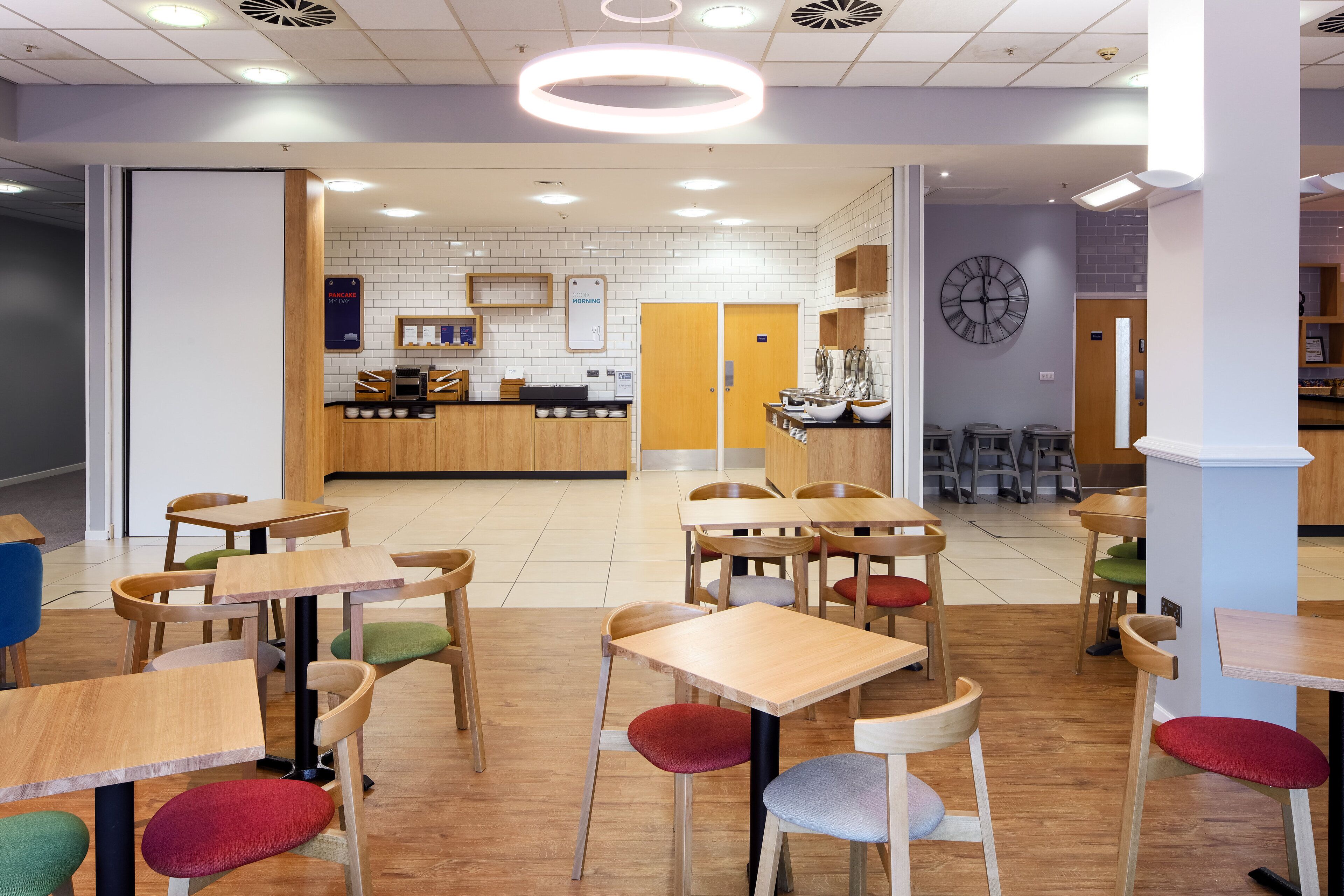 A modern restaurant with wooden tables and chairs, a counter, and a clock on the wall.
