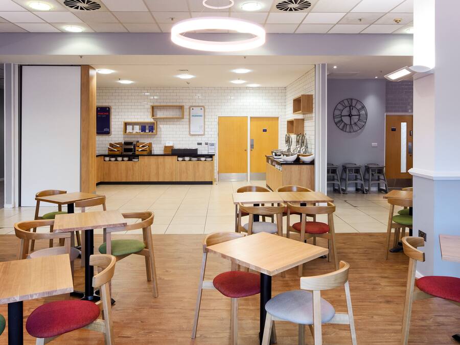 A modern restaurant with wooden tables and chairs, a counter, and a clock on the wall.